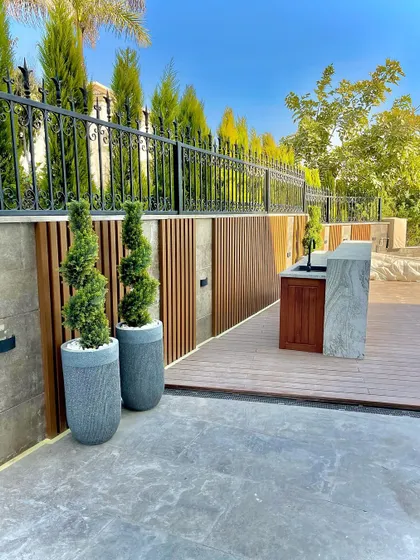 A modern rooftop or patio space featuring composite decking, a wood-slatted privacy screen, and contemporary planters. We use a mix of materials to create a functional and stylish outdoor area.