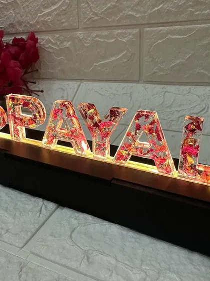 A close-up on the resin letters, where you can see the preserved red and pink flower petals that give the names color and texture.