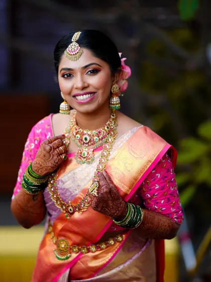 A portrait of the bride looking radiant in her pink and gold saree, her smile full of happiness.