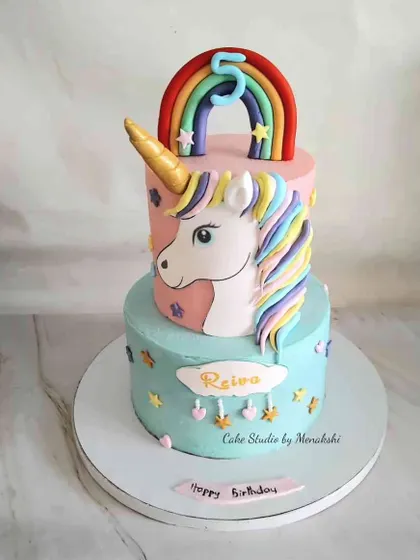 A magnificent two-tier unicorn cake for a 5th birthday. The bottom tier is a lovely pastel blue, while the top tier features a beautiful unicorn head with a colorful mane.