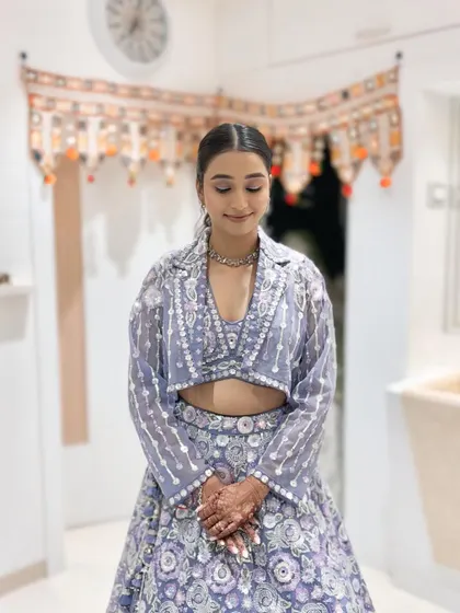 The makeup is kept fresh and minimal, with a focus on clean skin and defined eyes, perfect for her stylish lavender outfit.