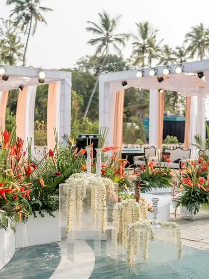 A poolside setup featuring elegant white and blush draped cabanas, accented with vibrant tropical flowers. The design includes unique floral installations floating in the water.