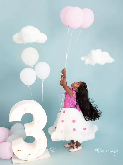 Floating into her third year. This whimsical birthday portrait features the birthday girl holding pink balloons, surrounded by fluffy clouds and a light-up number three.