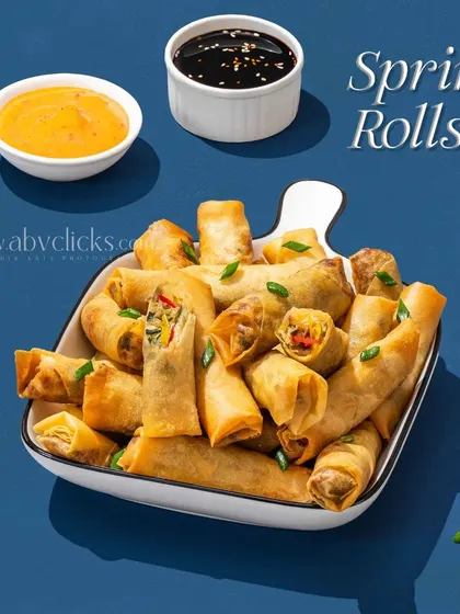 A bowl of spring rolls served with two dipping sauces, shot against a solid blue background for a modern look.