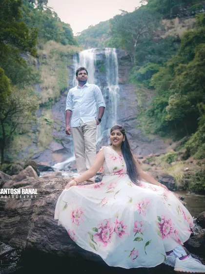 An elegant pose with the bride sitting on a rock, her dress spread out, with the groom standing behind her.