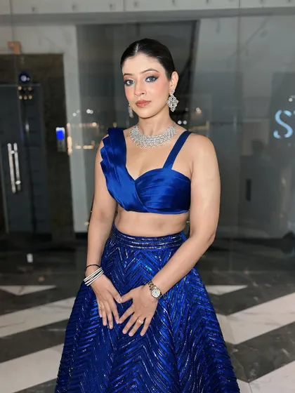 A full portrait of the client in her blue outfit. The sleek hair and bold outfit are balanced by the classic, clean makeup.