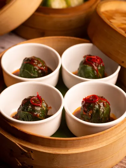 Steamed dumplings in individual serving bowls, garnished with chili. The presentation is elegant and the close-up shot makes them look very appetizing.