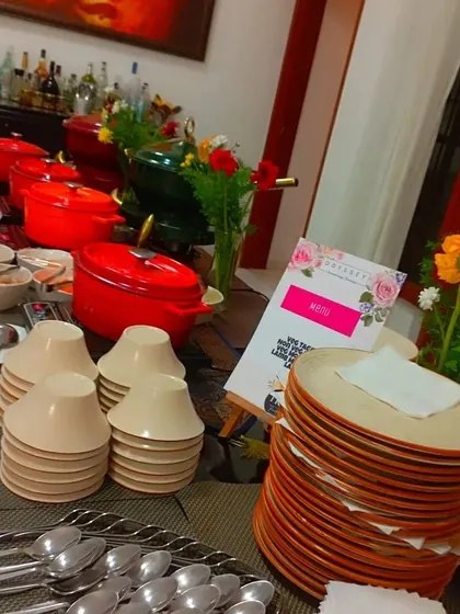 A full buffet table setup with stacked plates, cutlery, and colorful pots, ready for a party. We ensure your event is equipped with everything needed for a seamless dining experience.