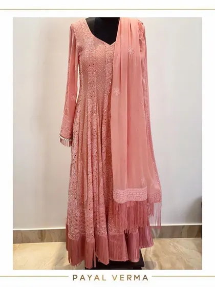 A studio shot of an elegant pink Anarkali. This piece features opulent Lakhnavi work all over and is detailed with thread tassels and pearls for a delicate finish.