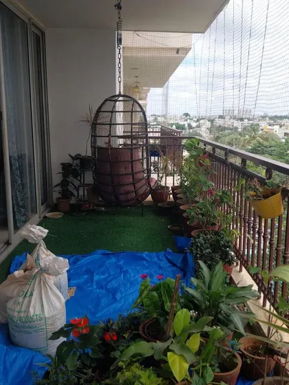 A work-in-progress shot of a balcony makeover. A hanging swing chair is installed over artificial turf, with new plants waiting on a blue tarp, ready to be arranged into a cozy green corner.