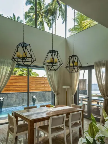 A double-height dining room in our Goa project, with large geometric chandeliers that draw the eye upward to the skylight. The space is flooded with natural light, and the view of the pool and palm trees makes every meal feel like a vacation.