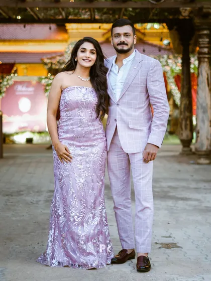 A beautiful couple, Divya and Aravind, in coordinated custom outfits. She wears a lavender sequined gown, and he a matching suit.