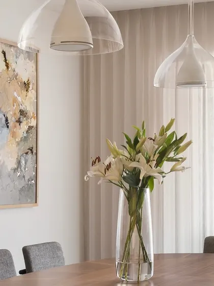 A close-up of the dining area in the West Coast Residence. The simple, clear glass pendant lights and a vase of fresh lilies create a feeling of calm and understated elegance.