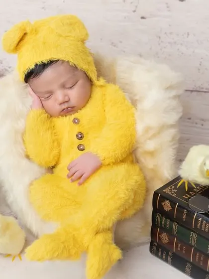 Dressed in a fuzzy yellow teddy bear outfit, this newborn is just adorable.