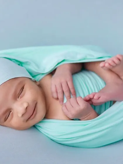 A happy, smiling baby in a mint green swaddle. Capturing these sleepy smiles is a matter of patience and creating a comfortable studio environment.