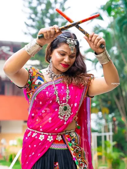 An energetic portrait of a woman dressed for Garba. Her pose with dandiya sticks held high captures the dynamic spirit of the Navratri dance festival.