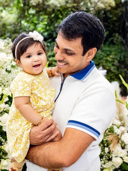 A proud father holds his smiling baby girl. This black and white portrait against a floral backdrop is simply picture-perfect.