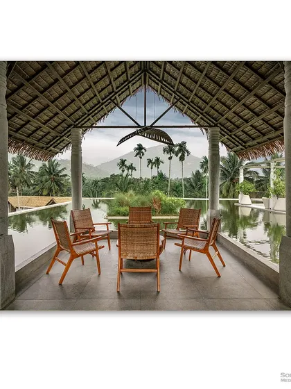Looking out from a tranquil seating area at Maayaa Resorts in Anaikatti, this photograph frames the majestic mountains through stone pillars. The thatched roof and serene infinity pool create a seamless connection between the architecture and the breathtaking natural landscape, promising a peaceful escape.