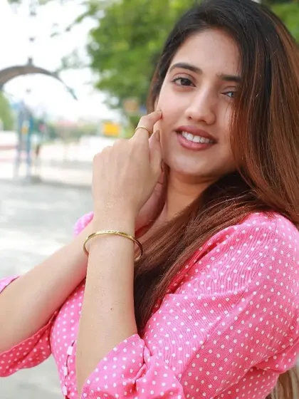 Another view of the woman in pink, touching her face and showing off the delicate gold cuff on her wrist.