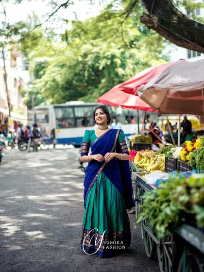 A shot from a market-themed shoot, wearing a Kanchi cotton half-saree. The vibrant colors of the vegetables and flowers complement the blue and green of the outfit.