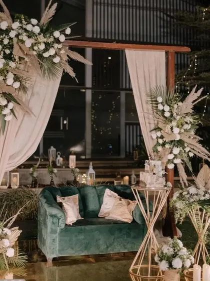 A stunning example of our bohemian-luxe style. This wedding reception stage features a rich green velvet sofa, dramatic pampas grass arrangements, and warm lighting, creating a cozy yet incredibly chic atmosphere.