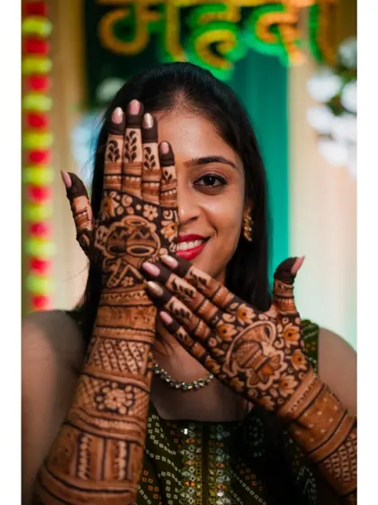 The bride playfully peeks through her hands, showing off her elaborate henna design. This is a fun and classic pose for a mehendi ceremony.