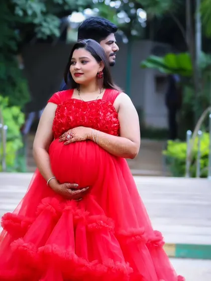 A beautiful profile shot of an expectant mother in a red ruffled gown, posing on a bridge in a garden.