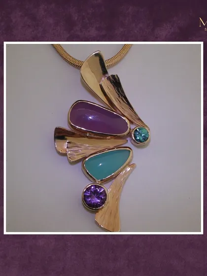 I love working with color. This bold, abstract pendant combines the calming energy of turquoise with the royal allure of purple gemstones, all set in textured yellow gold. It's a unique statement piece.