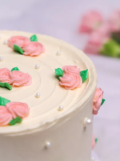 We believe in the timeless beauty of simplicity with this elegant floral cake. A pristine white buttercream canvas is adorned with delicate, hand-piped pink rosebuds and tiny pearls, creating a classic and graceful design perfect for Mother's Day or an anniversary.