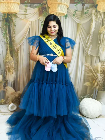 A stunning studio portrait of a mom-to-be in a flowing blue gown, holding tiny baby shoes. We offer styled maternity sessions complete with gowns and a beautiful setup.