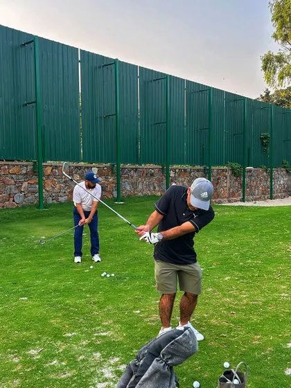 Two golfers work on their short game, one chipping while the other prepares to swing.