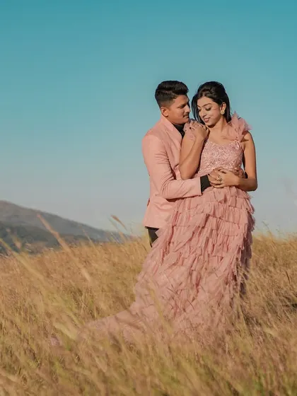 A couple shares an intimate moment in a field of tall grass, with a mountain range in the background. This style of outdoor pre-wedding photography captures a sense of adventure and romance.
