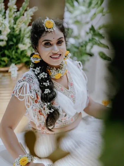 A stunning portrait of the bride in her white Haldi outfit, adorned with fresh yellow and white floral jewelry.