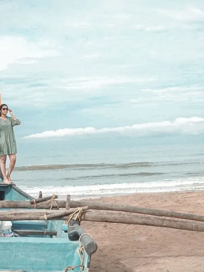 A relaxed and adventurous shot of the couple standing on a traditional fishing boat on a Goan beach, looking out at the sea.