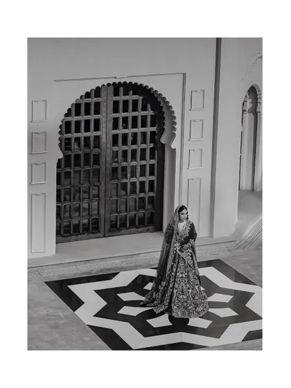 A timeless black and white portrait of the bride in her full lehenga, standing on a geometric-patterned floor.