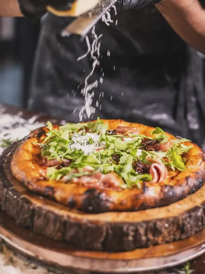 A final shower of freshly grated Parmesan cheese rains down on a Prosciutto and Arugula pizza. It's the finishing touch that adds another layer of authentic Italian flavor.