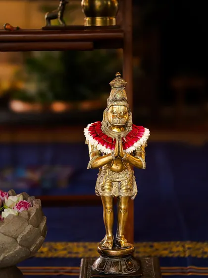 A brass statue of Hanuman, adorned with a red and white floral garland. Selecting and styling such divine figures with care is an important part of creating a respectful and sacred ambiance for traditional events.