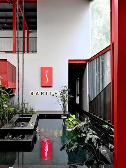 This marketing office interior for Saritha Serene demonstrates a bold use of color and industrial materials. The vibrant red staircase and structural elements contrast with the calm of the indoor water feature and plantings, creating a dynamic and memorable brand experience.