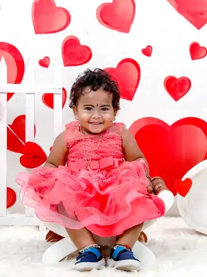 Celebrating love with a Valentine's Day themed photoshoot. This sweet little girl is all smiles in a pink dress, surrounded by a backdrop of red and white hearts.