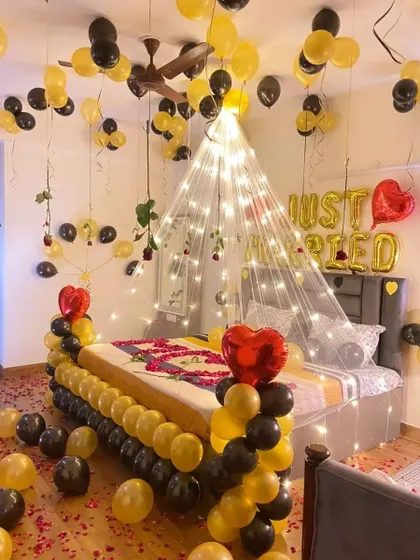 A "Just Married" first-night room decoration with a canopy of fairy lights, black and gold balloons, and rose petals.