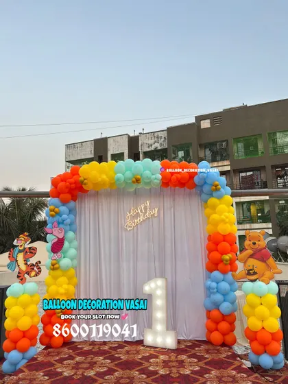 A colorful Winnie the Pooh themed first birthday. This outdoor setup features a vibrant balloon arch and character cutouts of Pooh and Tigger.