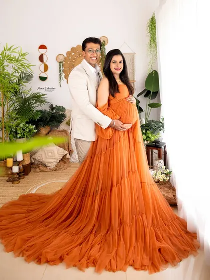 A classic couple's portrait where both partners gently hold the baby bump. The flowing orange gown adds a beautiful pop of color to this loving image.