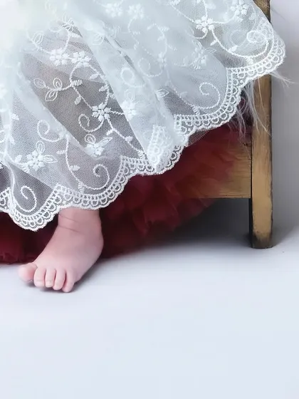A sweet detail shot of a newborn's foot peeking out from under a delicate white lace dress. It’s a subtle and beautiful way to capture their tininess.
