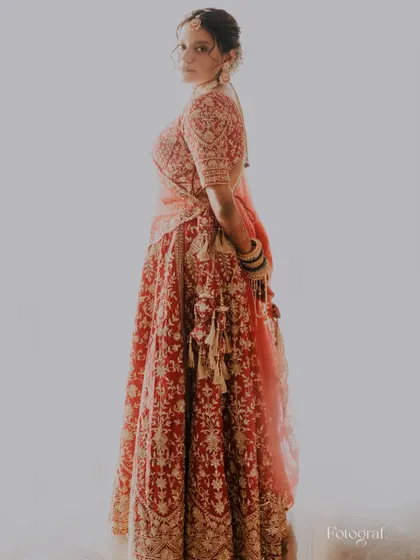 A classic, elegant bridal portrait against a clean white background, showcasing the intricate details of her red lehenga.