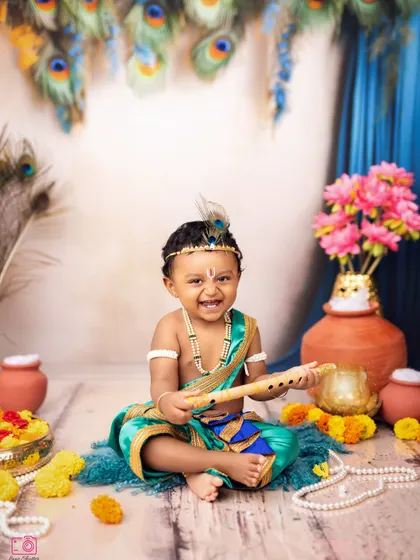 Another happy portrait of the baby boy dressed as Krishna, holding his flute with a big smile.