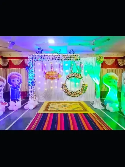 A naming ceremony decoration with light-up character cutouts and a hanging floral cradle. The colorful lighting adds a magical touch to the event.