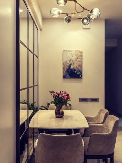 A cozy dining nook perfect for smaller spaces. This setup includes a compact marble-top table, comfortable upholstered chairs, and a large grid-style mirror that creates an illusion of a larger area.