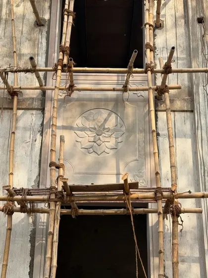 A beautifully carved stone panel framed by bamboo scaffolding. This image captures the essence of the project: the meeting of traditional craftsmanship and the raw, honest process of construction.