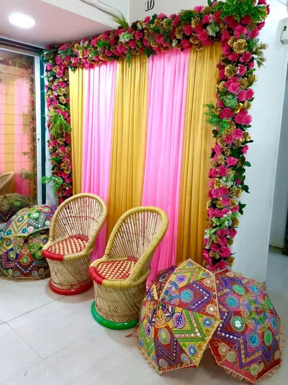 A vibrant photo corner for a Mehandi or Haldi event. I used pink and yellow drapes, a floral border, and traditional mooda chairs with colorful umbrellas to create this spot.