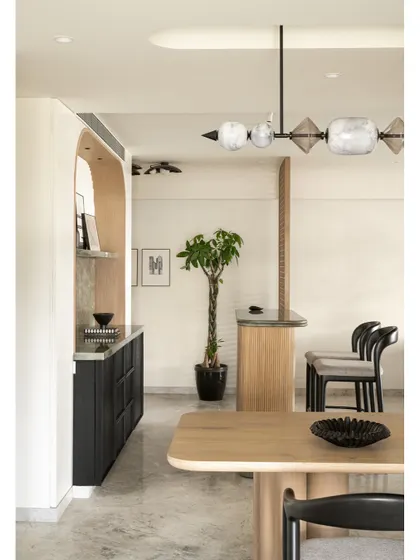 An overview of the dining and bar area in the Noir Blanc House, showcasing the sculptural chandelier, oak dining table, and the elegant bar setup in the background.